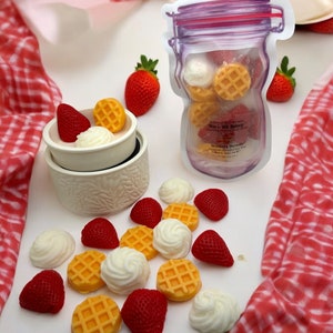 May include: A white ceramic wax warmer with a strawberry and waffle design wax melt. The wax melt is in a clear jar with a purple lid and the text "Wax & Wick Bakery" and "Strawberry Shortcake".