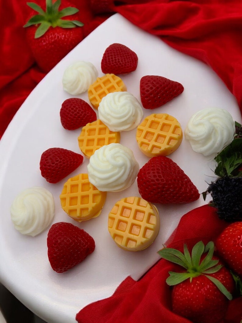 May include: A white plate with a variety of yellow waffle-shaped candies and red strawberries. The plate is surrounded by a red fabric.