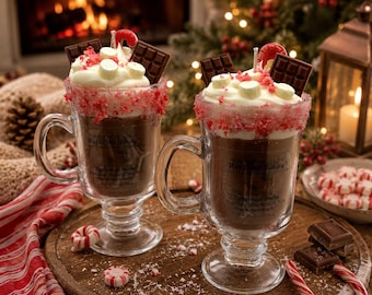 May include: Two glass mugs filled with brown wax resembling hot cocoa, topped with white wax whipped cream, chocolate squares, marshmallows, and a red candy cane. The rim is coated in red sugar crystals. Each mug features a label reading Peppermint Mocha.