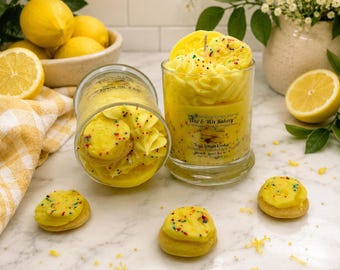 May include: A clear glass candle jar filled with yellow wax shaped like piped frosting and topped with small cookie-like wax pieces and colorful sprinkles. The label reads Wax & Wix Bakery and Iced Lemon Cookie. Two similar candles are visible.