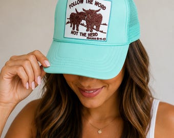 May include: A turquoise trucker hat with a mesh back and a curved brim. The front patch features two brown bulls and the text "FOLLOW THE WORD NOT THE HERD ISAIAH 6:11-13" in a white rectangle.