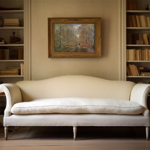 May include: A white sofa with a curved back and wooden legs sits in a room with two white bookshelves filled with books. A framed painting of a forest path hangs on the wall above the sofa.