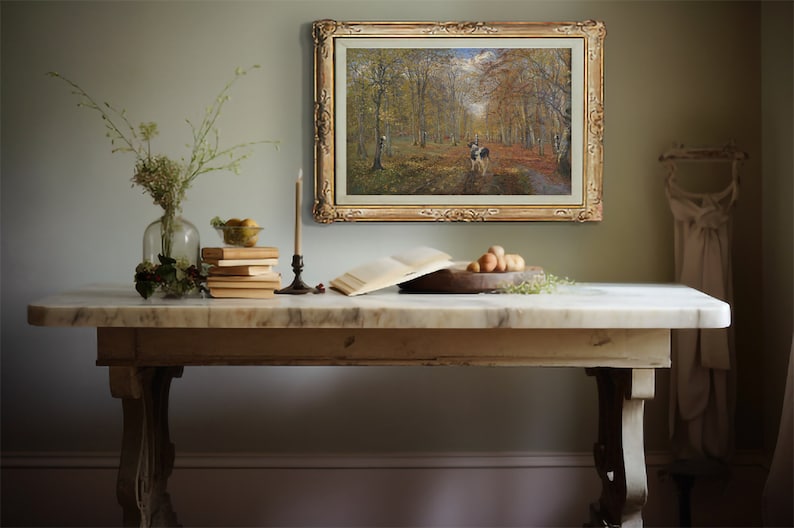 May include: A rustic wooden table with a white marble top. A framed painting of a forest scene hangs on the wall behind the table. A vase of flowers, a stack of books, and a bowl of fruit are on the table.