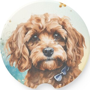 May include: Round car coaster featuring a watercolor illustration of a brown Cavapoo dog with a blue bow tie. The coaster has a light blue, yellow, and white background. The dog has brown fur and dark eyes.