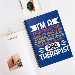May include: A blue spiral notebook with the text "I'm a Data Collecting Behavior Analyzing Environment Manipulation Reinforcement Loving Antecedent Solving ABA Therapist" in colorful text.