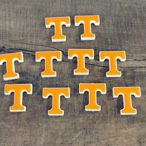 May include: Ten orange and white letter T's on a wood background. The letter T's are in a pyramid shape.