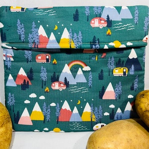 May include: A green fabric lunch bag with a repeating pattern of mountains, trees, and camper vans. The bag is folded in half and has a yellow seam.