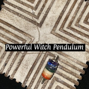 May include: A silver chain with a crystal pendulum featuring a stack of seven colourful stones. The stones are red, orange, yellow, green, blue, purple, and white. The pendulum is on a white and brown patterned surface. "Powerful Witch Pendulum" is written in black text on the surface.