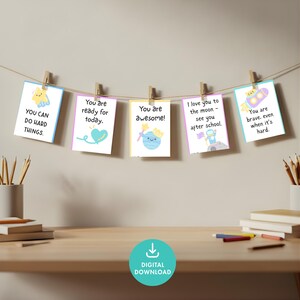 May include: A string of five colorful cards with positive affirmations, clipped to a string with wooden clothespins. The cards have illustrations of a star, heart, planet, astronaut, and rocket ship, with encouraging phrases.