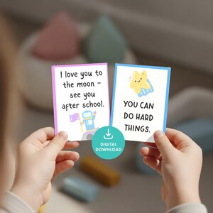 May include: Two cards with encouraging messages are held up. One card has the text "I love you to the moon - see you after school" with an astronaut graphic. The other card says "YOU CAN DO HARD THINGS" with a star graphic. A digital download icon is also visible.