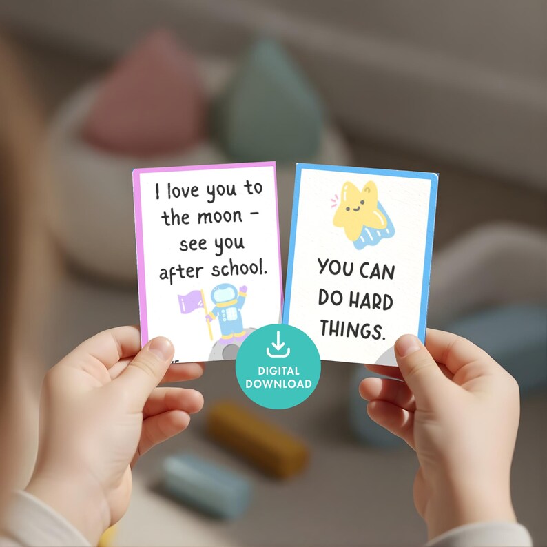 May include: Two cards with encouraging messages are held up. One card has the text "I love you to the moon - see you after school" with an astronaut graphic. The other card says "YOU CAN DO HARD THINGS" with a star graphic. A digital download icon is also visible.