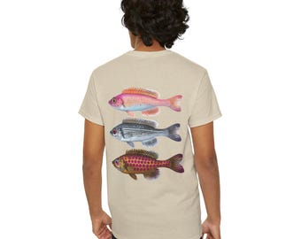 Puede incluir: Una camiseta beige de manga corta con un estampado gráfico en la espalda de tres peces distintos apilados verticalmente. El pez superior es rosa con detalles naranjas, el del medio es plateado con rayas oscuras y el inferior es marrón con manchas moradas.