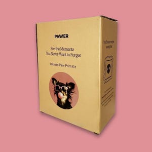 May include: A rectangular cardboard box for an inkless paw print kit. The front features the text PAWER, For the Moments You Never Want to Forget, Inkless Paw Print Kit, and a circular image of a dog wearing pink sunglasses blowing a bubble.