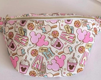 May include: A pink and white fanny pack with a zipper closure. The fanny pack has a repeating pattern of Mickey Mouse ears, popcorn buckets, ice cream cones, and other Disney-themed snacks. The text "Magic" appears on some of the tickets in the pattern.