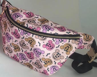 May include: Pink fanny pack with a repeating pattern of Mickey Mouse-shaped jack-o'-lanterns in orange, pink, and purple. The bag has a black zipper and strap with a gold-colored buckle. Small black bat silhouettes are scattered throughout the design.