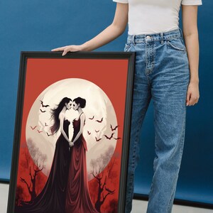 May include: Framed art print featuring two women in long dresses standing in front of a full moon with bats flying around them. The background is a red and orange gradient with trees.