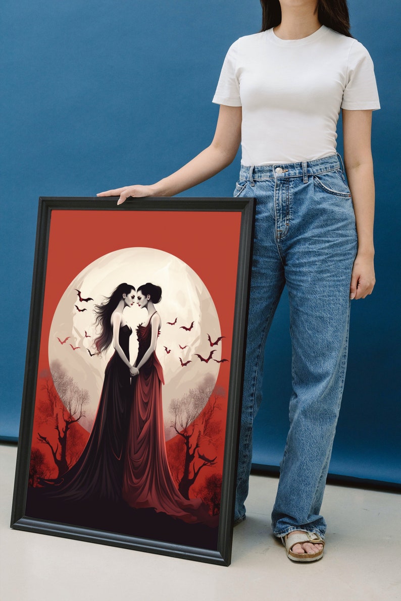 May include: Framed art print featuring two women in long dresses standing in front of a full moon with bats flying around them. The background is a red and orange gradient with trees.