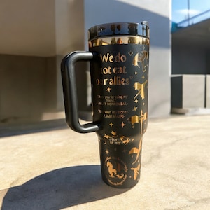 May include: Black travel mug with a gold design featuring dragons and the text "We do not eat our allies". The text "Thank you for being my friend." is also included with the name "ACET SORRENGAIL" and "It's been my honor." with the name "LIAM MAIRI".