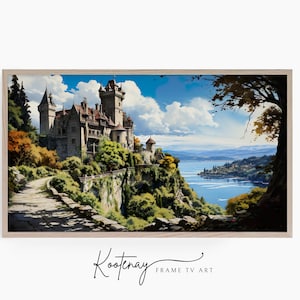 Op de afbeelding: Een ingelijste digitale kunstprint met een kasteel op een klif met uitzicht op een meer. De afbeelding toont een stenen pad, weelderig groen en een helderblauwe lucht met wolken. De lijst is licht houtkleurig. De tekst "Kootenay FRAME TV ART" staat onderaan.
