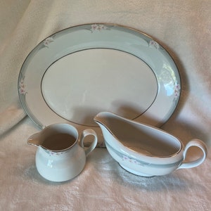 May include: A set of three white porcelain dishes with a floral design. The set includes a large oval platter, a gravy boat, and a creamer.