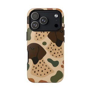 May include: A phone case featuring a repeating pattern of a dog's head and body in brown and tan. The case has a beige background with green and brown abstract shapes. The phone case has a black camera module.