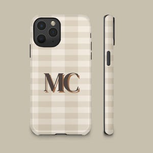 May include: A phone case featuring a beige and white checkered pattern with the letters MC printed in a dark brown serif font in the center. The case includes a black camera cutout and a side view showing the slim profile and black side buttons.