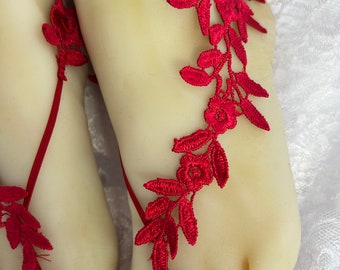 May include: Red lace foot jewelry with floral designs. The jewelry is tied around the ankles and feet with red ribbon.