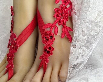 May include: Red lace barefoot sandals with floral embellishments. The sandals are tied around the ankle and have a delicate, feminine design.
