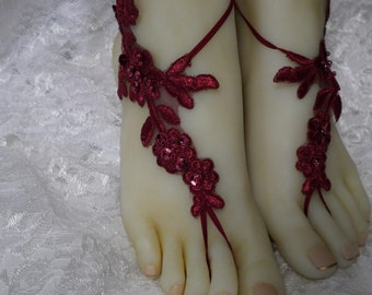 May include: Burgundy barefoot sandals with floral lace and sequin accents. The sandals feature a delicate design with a toe loop and ankle ties. Perfect for weddings, beach events, or special occasions.