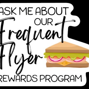 K&ouml;nnte beinhalten: Wei&szlig;er Aufkleber mit schwarzem Text, der "Fragen Sie mich nach unserem Frequent Flyer Rewards Programm" lautet. Auf dem Aufkleber ist ein Cartoon-Sandwich mit Salat, Tomate, Zwiebel und K&auml;se abgebildet.