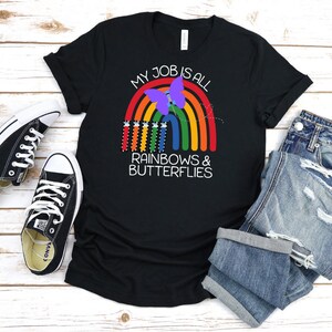 May include: Black t-shirt with a rainbow and butterfly design. The text on the shirt reads "My job is all rainbows & butterflies".