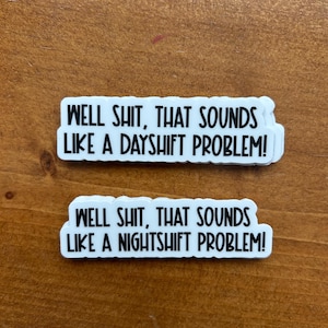 May include: Two white stickers with black text on a wooden surface. The top sticker reads "WELL SHIT, THAT SOUNDS LIKE A DAYSHIFT PROBLEM!". The bottom sticker reads "WELL SHIT, THAT SOUNDS LIKE A NIGHTSHIFT PROBLEM!"