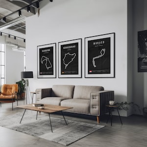 May include: Three black framed prints of race tracks, Silverstone, Nurburgring, and Monaco, hang on a white wall above a gray sofa in a modern living room.