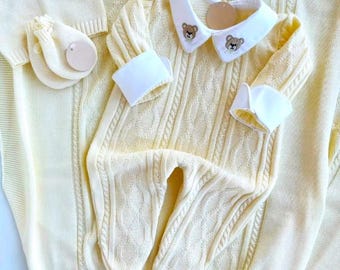 May include: A yellow knitted baby onesie with a white collar and bear embroidery. The onesie has a cable knit pattern and is part of a matching set with a hat and mittens.