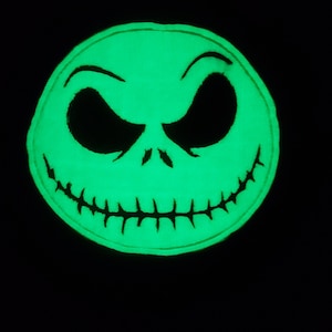 Pode incluir: Um remendo verde que brilha no escuro com o rosto de Jack Skellington do filme "O Estranho Mundo de Jack".