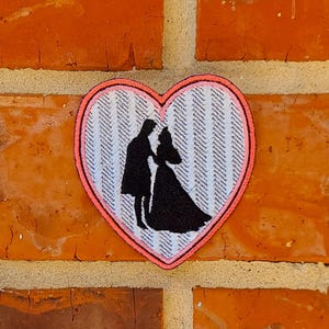 May include: A pink heart-shaped patch with a white and gray chevron pattern. The patch features a silhouette of a couple in a wedding dress and suit.