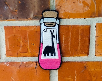 May include: A pink glass bottle with a cork stopper and a white label featuring a black silhouette of a llama. The label also has a white rectangle with a black outline.