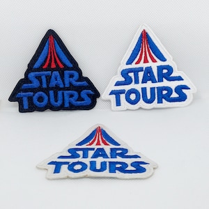 Op de afbeelding: Drie geborduurde patches met het Star Tours logo. Het logo is een witte driehoek met een rood en blauw ruimtebergontwerp. De tekst "STAR TOURS" staat in blauwe letters.