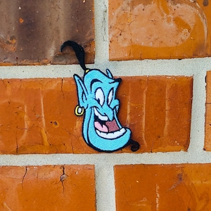 May include: A blue genie with a mischievous grin and a black turban, embroidered on a brick wall.