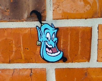 May include: A blue genie with a mischievous grin and a black turban, embroidered on a brick wall.