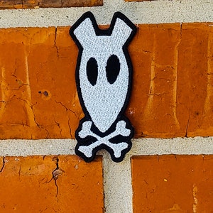 May include: White embroidered patch of a ghost with black eyes and a skull and crossbones design.