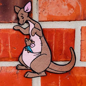 May include: Embroidered patch featuring Kanga from Winnie the Pooh, a brown kangaroo with a pink pouch, holding Roo, a small brown joey, in her pouch.