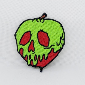 May include: A green apple with a red skull face and dripping red and green liquid. The apple is embroidered on a white background.