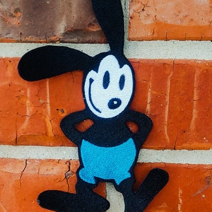May include: A black and white cartoon character with large ears and a blue shirt. The character is standing on a brick wall.