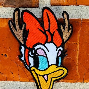 Op de afbeelding: Een geborduurde patch met een cartoon eend met geweien. De eend is rood, wit en geel met grote blauwe ogen, een gele snavel en een roze blos op zijn wangen.