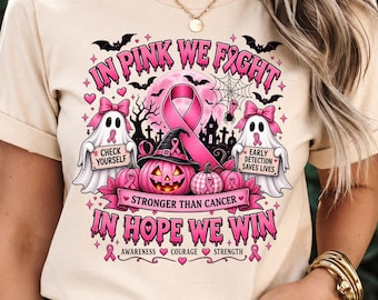 Puede incluir: Una camiseta beige con un gráfico de dos fantasmas, una calabaza y un lazo rosa de concienciación sobre el cáncer de mama. El texto dice IN PINK WE FIGHT, CHECK YOURSELF, EARLY DETECTION SAVES LIVES, STRONGER THAN CANCER, IN HOPE WE WIN.