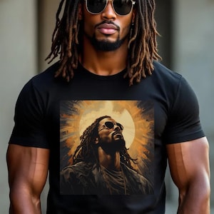 A Black man with dreadlocks wearing a black t-shirt featuring a bold graphic of Black Jesus with sunglasses, surrounded by a golden halo-like design. The man stands confidently in an urban setting, exuding strength and faith.