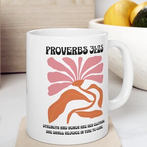 May include: White ceramic mug with a pink and orange floral design. The mug features the text "PROVERBS 31:25" and the quote "STRENGTH AND HONOR ARE HER CLOTHING, SHE SHALL REJOICE IN TIME TO COME."