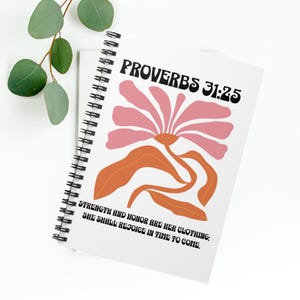 May include: A white spiral notebook with a pink and orange floral design. The cover features the text "PROVERBS 31:25" and the quote "STRENGTH AND HONOR ARE HER CLOTHING: SHE SHALL REJOICE IN TIME TO COME."
