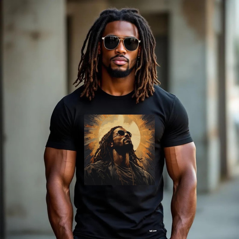 A Black man with dreadlocks wearing a black t-shirt featuring a bold graphic of Black Jesus with sunglasses, surrounded by a golden halo-like design. The man stands confidently in an urban setting, exuding strength and faith.